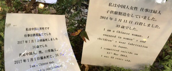 植え込みの中のプラカ。「私は中国人男性です　仕事は鉄筋施工でした　2017年1月1日頃溺死しました　36歳でした」「私は中国人女性　仕事は婦人子供服製造をしていました。2014年5月11日　自殺しました。33歳でした」といった文章が日本語・英語・中国語で書かれている