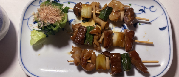 各種ホルモン・ねぎま風に短く切った長ネギ・オクラ・ぶなしめじを串に通して甘辛しょうゆダレでこんがりめに焼き上げた串と、かつおぶしを振った小松菜のおひたし。